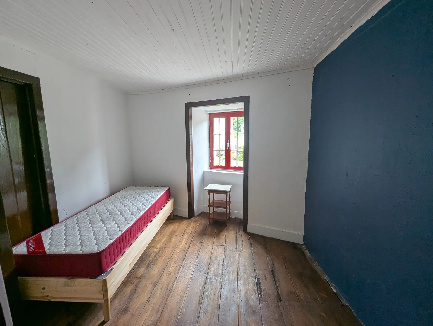 Quarto com pavimento em madeira e janela vermelha